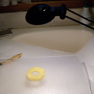 Kitchen sink, cutting board, with pineapple slice on it and desk lamp