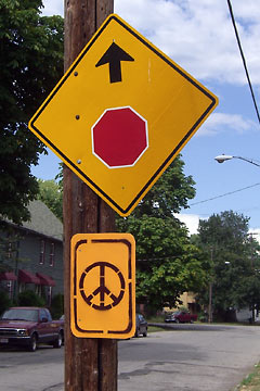 Stencilled peace sign on pole below official traffic sign