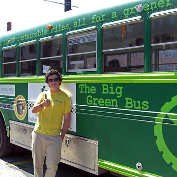 Student standing next to Big Green Bus giving thumbs up sign