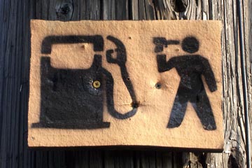 Hand-stenciled sign showing gas pump and man with gun to his head