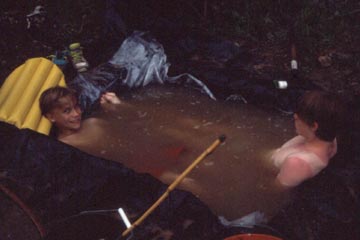 Two boys in hole  dug in ground, filled with water.