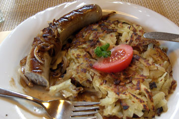Plate of rosti with bratwurst, topped by tomato slice