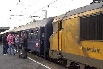 Dirty yellow train engine with group of people standing on platform alongside