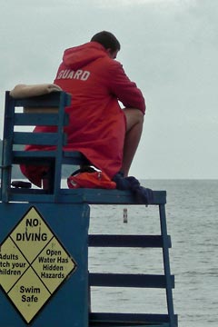 Lifeguard wearing red parka sitting on top of chair