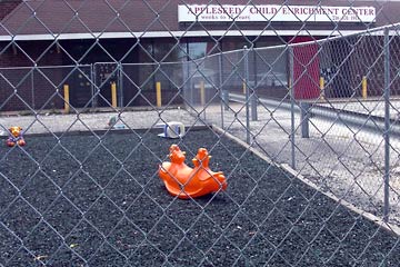 View through fence toward dark, barren play area