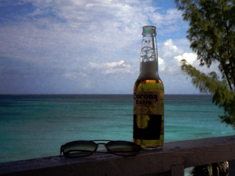 Corona beer bottle, sunglasses on porch in front of turquoise sea