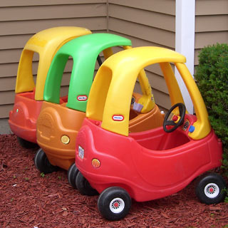 Three LIttle Tykes toy cars lined up in a row outside the house