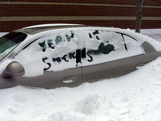 Car buried in snow with yeah it sucks written in snow