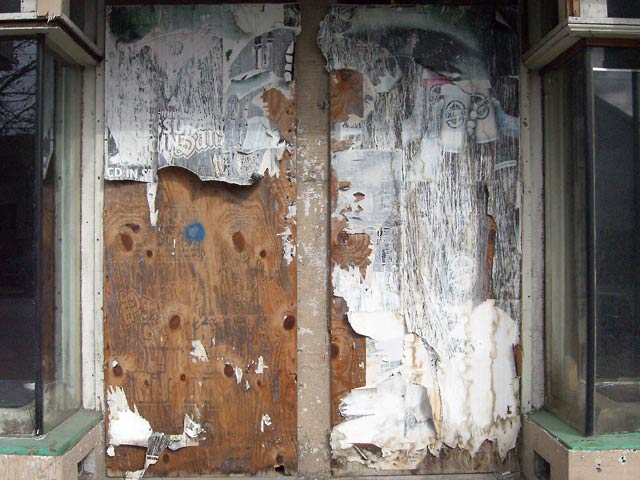 Storefront with boarded up doors, torn posters