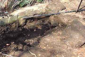 Trench filled with dirt, big rock alongside