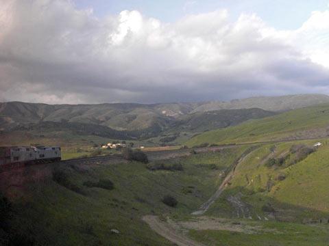 Train going around a curve with green hills in the background