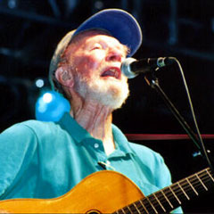 Pete Seeger in a turquoise shirt, singing and playing guitar