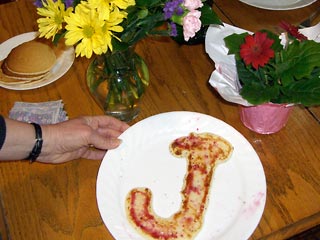 Pancake in the shape of a J, surrounded by flowers.