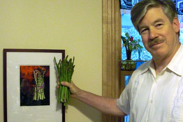 Jack holding a bunch of asparagus next to photo of asparagus