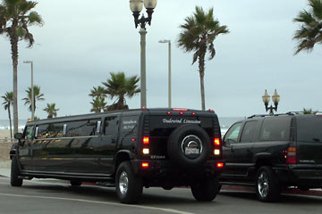 Huge black Hummer limo and black GMC Yukon parked near beach