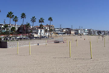 Wide stretch of sandy beach with volleyball nets; house and palm trees in the distance