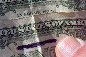Dollar bill with "In God We Trust" marked out in black