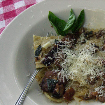 White bowl with sauteed mushroom and tomatoes over ravioli