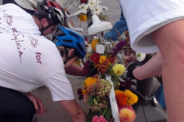 People placing brightly-colored flowers on white bicycle.